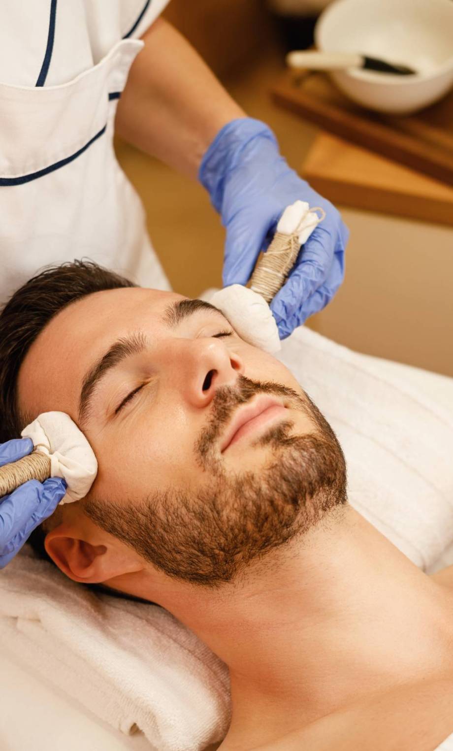 Young man receiving head massage with herbal balls at the spa. Relaxed man having Thai herbal head massage at wellness center.